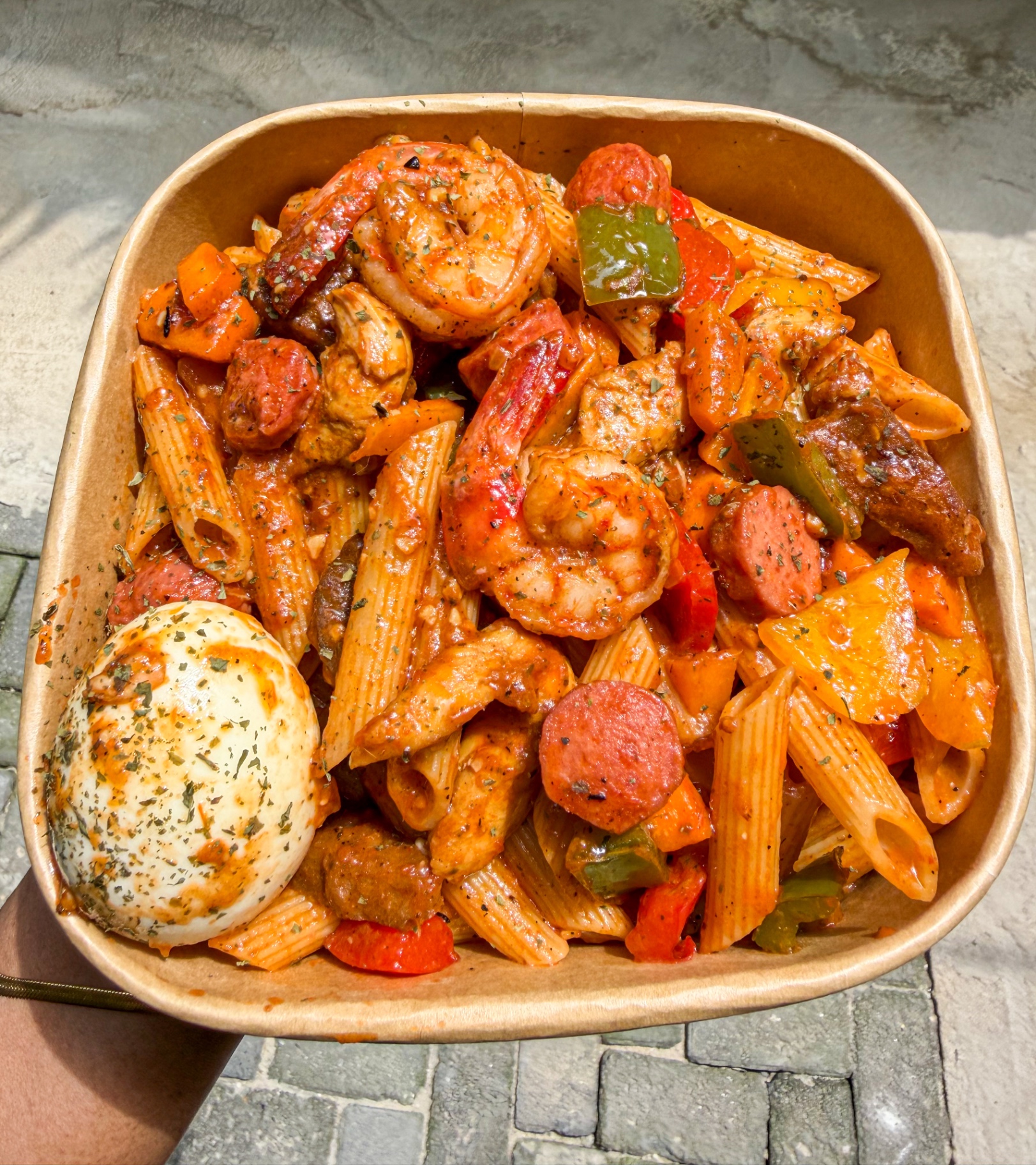 Penne with prawns, sausage, peppers and boiled egg in a paper bowl
